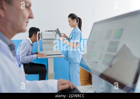 Infermiere oftalmico che utilizza attrezzature moderne per la diagnosi della malattia oculare del paziente Foto Stock