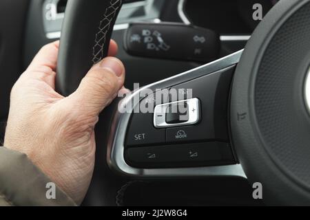 Pulsanti del controllo della velocità di crociera e del volume sul volante dell'auto moderna, dettagli interni con la mano del conducente Foto Stock