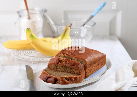 Pane fatto in casa pane di torta di Banana affettato su un tavolo primo piano. Verticale, stile rustico bianco, concetto di panetteria. Foto Stock