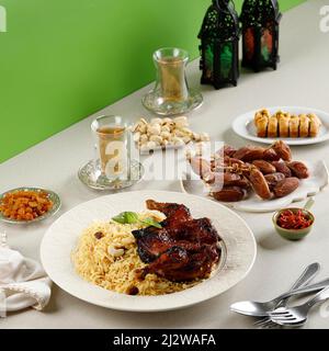 Menu a buffet di Iftar Ramadan, Kabsa di riso Basmati con pollo arrosto, raisina, tè, frutta datteri, pistacchio, E Baklava turco. Concetto di verde Foto Stock