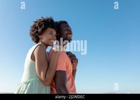 Sorridente coppia afroamericana in piedi guardando lontano contro il cielo blu chiaro con spazio copia Foto Stock