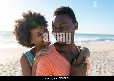 Felice afroamericana donna abbracciata ragazzo da dietro in spiaggia in giorno di sole Foto Stock