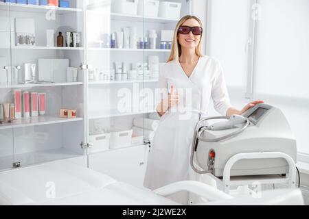 Allegro giovane donna beautician in piedi vicino a macchina di epilazione laser Foto Stock