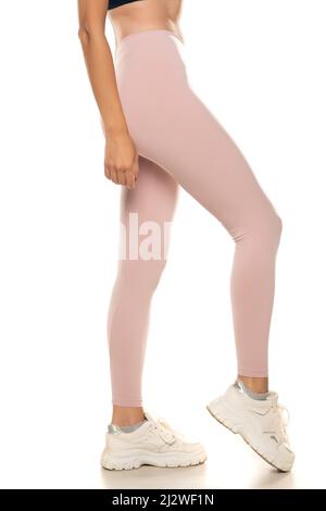 Vista laterale di una gamba femminile in tights rosa sportivo e sneakers su sfondo bianco. Foto Stock