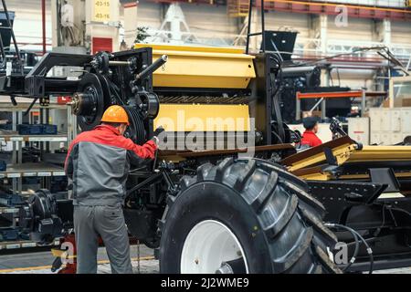 L'operatore monta la mietitrebbia per veicoli agricoli in un'officina industriale. Foto Stock