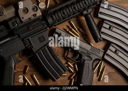 m4 fucile con vista ottica, pistola a mano, munizioni e cartucce su tavola di legno Foto Stock