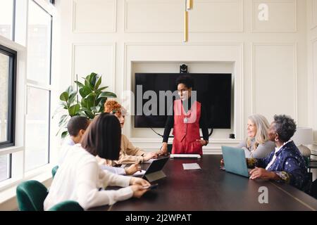 Ritratto di allegro uomo d'affari nero maturo discutere con le colleghe femminili nella sala riunioni Foto Stock