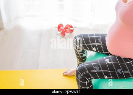 giovane donna incinta seduta su una palla fitness facendo sport per rimanere attiva in gravidanza Foto Stock