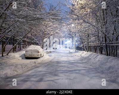 Mosca. Russia. Aprile 3, 2022. Vista notturna della strada nel parco durante una nevicata a Mosca. Le auto parcheggiate lungo la strada sono coperte di neve. Rami di albero sono coperti di neve. Foto Stock