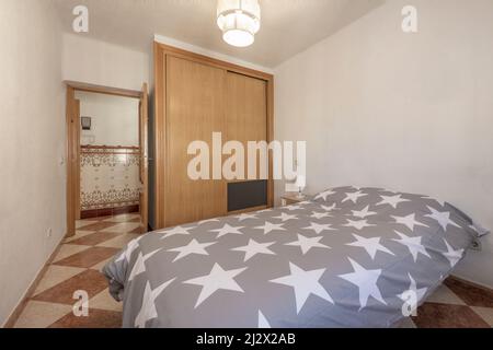 Camera da letto giovanile con trapunta grigia sul letto, armadio a muro con porte scorrevoli e pavimenti in ceramica Foto Stock