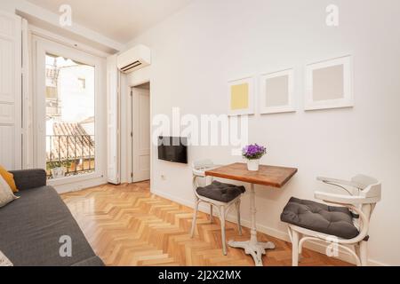 Soggiorno con tavolo in legno con piede in ghisa, sedie in legno bianco, balcone con ringhiera in metallo nero e vista sui tetti della città Foto Stock