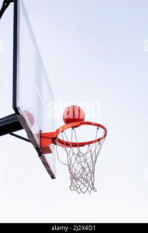 palla che entra in un cerchio di basket con il cielo sullo sfondo, concetto di sport urbano all'aperto, copia spazio per il testo Foto Stock