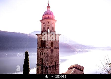 Chiesa Torre Santa Maria del Sasso con luce solare e montagna sul Lago di Lugano in Morcote, Ticino in Svizzera. Foto Stock