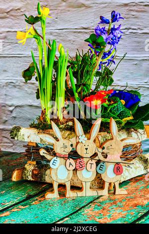 Composizione floreale con coniglietti pasquali in legno come decorazione e il testo Pasqua sulle uova di Pasqua. Foto Stock