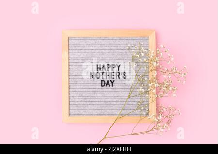 Buon giorno delle madri. Carta da lettere e fiori di gypsophila su sfondo rosa. Concetto festivo. Foto Stock