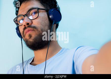 Ritratto di un ragazzo ispanico che indossa occhiali e cuffie su sfondo blu Foto Stock
