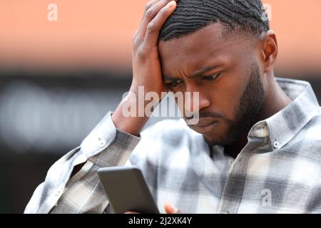 Uomo preoccupato con la pelle nera che lamenta il controllo del contenuto dello smartphone in strada