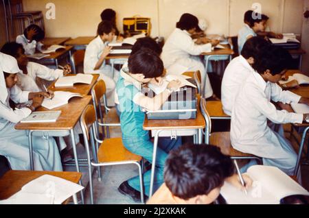 Arabia Saudita ex-pat Boy scrivere in classe appoggiandosi sul suo briefcase a scuola (anni '70) Foto Stock