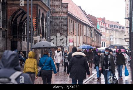 04 aprile 2022, Schleswig-Holstein, Lübeck: I passanti con e senza maschere camminano attraverso il centro della città sotto la pioggia. Lübeck ha modificato le regole della corona. (Alla dpa "Lübeck rimane per il momento con obbligo di maschera negli edifici comunali") (utilizzare solo in formato completo). Foto: Daniel Bockwoldt/dpa Foto Stock