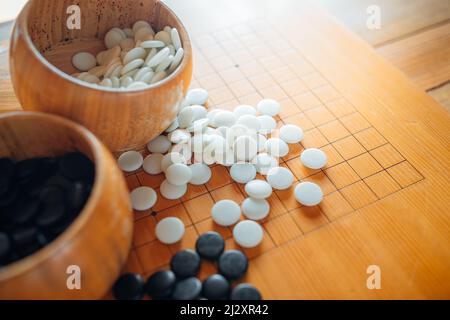 Un set di pietre da gioco Go o iGO nelle ciotole di legno sul tavolo a griglia. Foto Stock