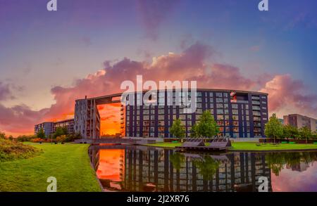 lago e campo verde vicino moderno edificio residenziale in via Tom Kristensens nella zona della città di Ørestad al tramonto. Copenaghen, Danimarca Foto Stock