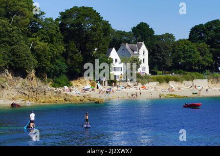 Fouesnant (Bretagna, Francia nord-occidentale): Spiaggia di Kerveltrec vicino a la Roche Percee in estate. Uomo e ragazzo, padre e figlio, paddleboard sul turquo Foto Stock