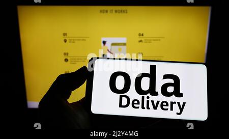 Persona che tiene il cellulare con il logo della società di logistica Saudita Oda Delivery sullo schermo di fronte al sito web aziendale. Mettere a fuoco sul display del telefono. Foto Stock