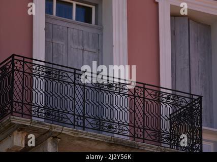 Antica casa neoclassica persiane finestre in legno grigio con un rivestimento bianco e un balcone con una ringhiera in ferro battuto su una parete in stucco veneziano in Grecia. Foto Stock