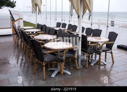 04 aprile 2022, Schleswig-Holstein, Lübeck-Travemünde: Tavoli e sedie assemblati si trovano sotto la pioggia sul lungomare del Mar Baltico. Foto: Daniel Bockwoldt/dpa Foto Stock