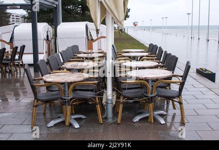 04 aprile 2022, Schleswig-Holstein, Lübeck-Travemünde: Tavoli e sedie assemblati si trovano sotto la pioggia sul lungomare del Mar Baltico. Foto: Daniel Bockwoldt/dpa Foto Stock