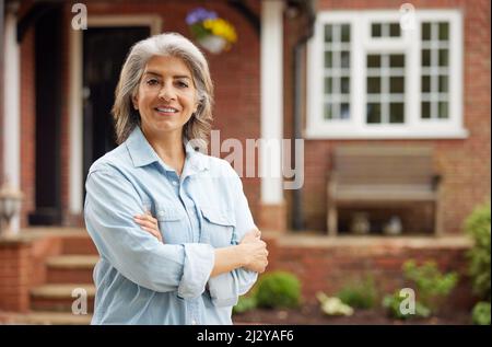 Ritratto di donna matura in piedi nel giardino davanti a casa da sogno in campagna Foto Stock