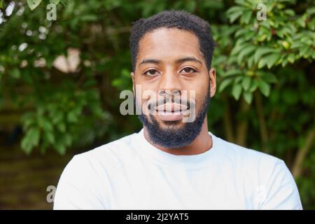 Testa e spalle Ritratto di sorridente giovane uomo in piedi all'aperto in giardino Foto Stock