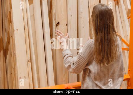 Donna che sceglie asse di legno nel deposito di ferramenta. Materiali da costruzione per il rinnovo della casa Foto Stock