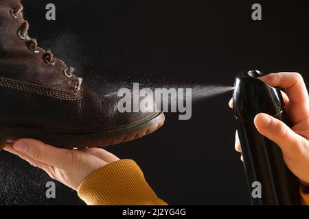 Una donna applica lo spray agli stivali invernali marroni nabuk da donna. Cura idrorepellente delle scarpe, rinnovamento e conservazione del colore Foto Stock