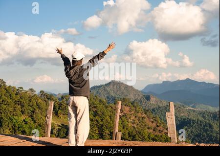 Allegra vista posteriore di donna asiatica in piedi braccia sollevate su balcone di legno con cima di montagna nella campagna a Chiang mai, Thailandia Foto Stock