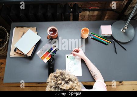 Vista ad angolo alto della giovane donna con braccio protesico usando acquerello e pennello per dipingere un'immagine a tavola Foto Stock