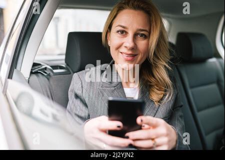 Una giovane donna d'affari si siede sul sedile posteriore di un'automobile ed usa il suo telefono. Foto Stock