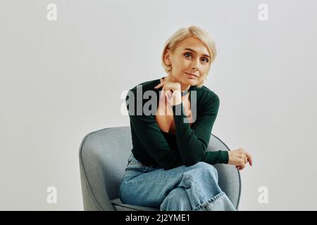 Ritratto minimale di giovane donna elegante guardando la fotocamera e sorridendo mentre si posa in studio, spazio copia Foto Stock