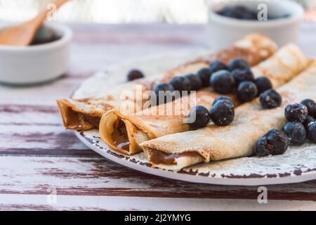 Delizioso piatto con pancake fatti in casa o crepes ripieni di dulce de leche e mirtilli e zucchero a velo che ricopre il piatto. Foto Stock