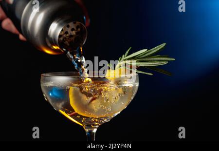 Gin tonico con rosmarino e limone. Il cocktail viene versato da uno shaker in un bicchiere. Foto Stock