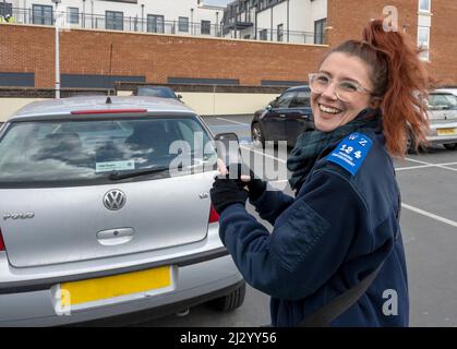 Happy at Work, un agente di controllo del parcheggio al lavoro in un parcheggio, Farnham, Surrey, Inghilterra, Regno Unito. Foto Stock
