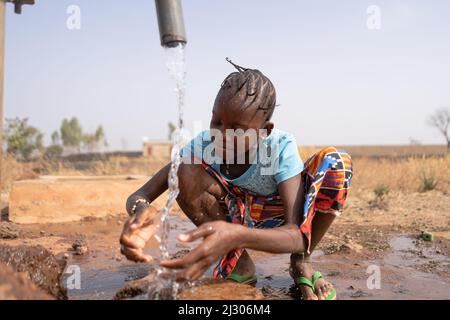 La ragazza africana assetata si rinfresca con acqua potabile fredda da un rubinetto villaggio; concetto di scarsità d'acqua, carenza d'acqua pancontinentale Foto Stock