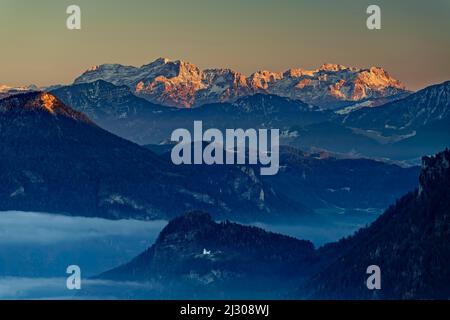 Atmosfera serale con nebbia a valle e vista di Petersberg con cappella, Madron e Loferer Steinberge, Montagne di Mangfall, Alpi bavaresi, alta Baviera, Baviera, Germania Foto Stock