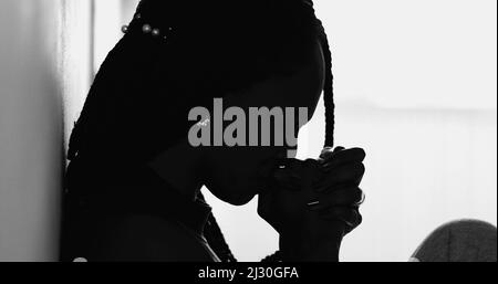 Donna religiosa africana in cerca di aiuto divino durante i tempi di lotta, silhouette nera femmina in preghiera Foto Stock