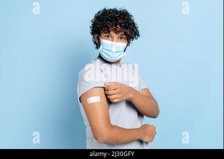 L'uomo indiano o arabo con maschera protettiva medica in faccia e con una fascia-aiuto sulla spalla, ha ricevuto un vaccino, protezione contro il covid 19, e l'uomo oindiano o arabo con maschera protettiva medica in Foto Stock