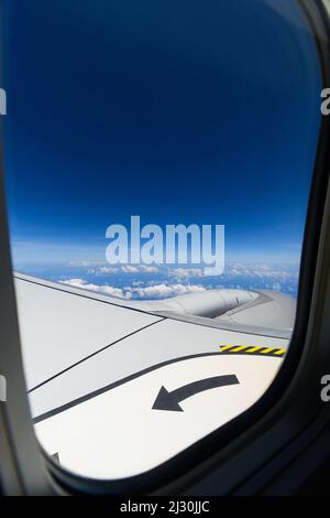 Vista attraverso la finestra di un aereo dell'ala e turbina durante un volo su una bella giornata di cielo blu con nuvole bianche, volare alto. Foto Stock