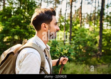 Giovane uomo che cammina con le racchette nei boschi durante l'escursione estiva Foto Stock