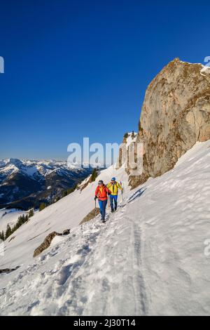 Uomo e donna che camminano fino al Rotwand attraverso il pendio di neve, torri di roccia sullo sfondo, Rotwand, Spitzing area, Alpi bavaresi, alta Baviera, Baviera, Germania Foto Stock