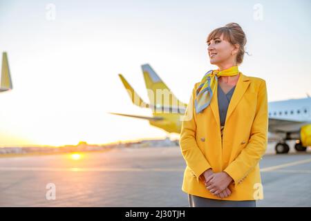 Gioioso assistente di volo donna in piedi all'aperto in campo aereo Foto Stock