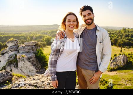 Ritratto di giovane coppia felice in piedi insieme con paesaggio di campagna dietro di loro durante l'escursione estiva Foto Stock